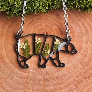 May include: A silver necklace featuring a bear-shaped pendant. The pendant is filled with pressed flowers and greenery.