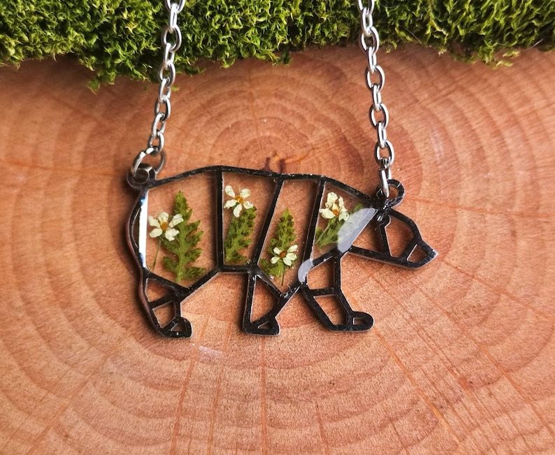 May include: A silver necklace featuring a bear-shaped pendant. The pendant is filled with pressed flowers and greenery.