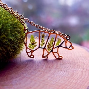 May include: A gold-toned necklace featuring a bear pendant. The bear is crafted from metal and has a geometric design. The bear is filled with pressed flowers and leaves.