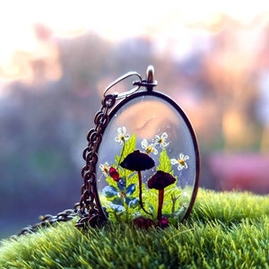 May include: A delicate necklace with a clear glass pendant containing tiny white flowers, green leaves, and two small mushrooms, one black and one brown.