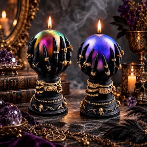 May include: Two spherical candles held by black sculpted hands with long fingers, adorned with gold rings and bracelets. The left candle has an iridescent green and purple finish, while the right candle is blue and purple. Both sit on black bases.