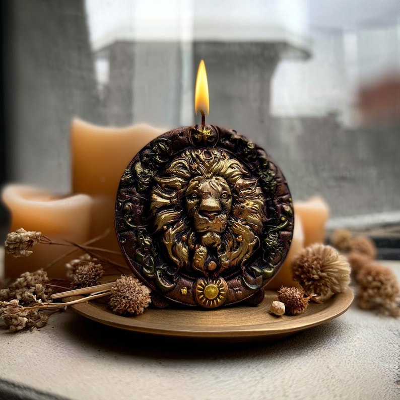 May include: A lit, decorative candle with a lion's head design. The candle is brown and gold, with a detailed lion's face in the center. It sits on a small, round, gold-colored plate, with dried flowers and other candles in the background.