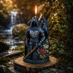 Könnte beinhalten: Eine dunkelblaue, skulptierte Kerze in Form einer Kapuzenfigur in Rüstung mit Schwert, einem Raben auf der Schulter und einer roten Rose an der Basis. Die Kerze hat einen brennenden Docht an der Spitze und zeigt detaillierte Verzierungen.