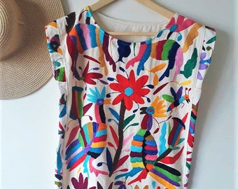 May include: A white cotton tunic with colorful embroidery of flowers, birds, and other designs. The embroidery is done in a variety of colors, including red, blue, green, yellow, and pink.