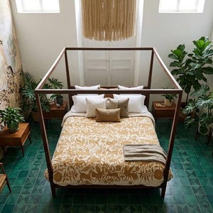 May include: A wooden four-poster bed frame centered in a room with green tiled flooring. The bed features a mustard yellow patterned quilt, white and tan pillows, and a gray throw blanket. Several potted green plants surround the bed frame.