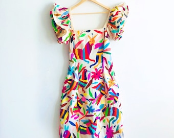May include: A white dress with colorful embroidered flowers and animals. The dress has puffed sleeves and a square neckline.