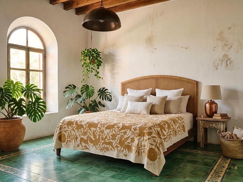 May include: A bed featuring a cream-colored quilt with a mustard yellow botanical and animal print pattern. The bed has a woven headboard and is layered with multiple neutral-toned throw pillows. A lamp sits on a wooden side table nearby.
