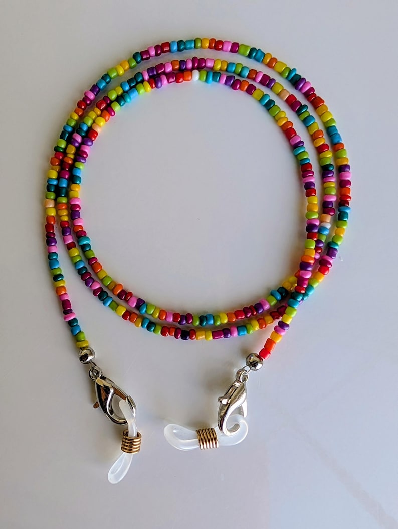 Puede incluir: Una cadena para gafas hecha de peque&ntilde;as cuentas de vidrio multicolores en tonos rojo, naranja, amarillo, verde, azul y morado. La cadena incluye cierres de mosquet&oacute;n plateados y bucles de silicona blanca con espirales de color dorado.