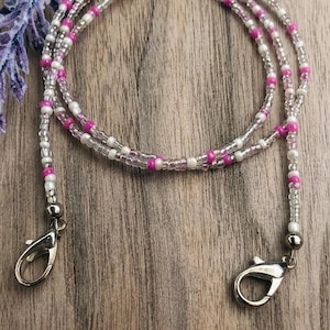 Puede incluir: Un cord&oacute;n de cuentas con un patr&oacute;n repetitivo de peque&ntilde;as cuentas redondas de color blanco opaco, transparente y rosa vibrante. El cord&oacute;n est&aacute; rematado con dos cierres de mosquet&oacute;n de metal plateado en cada extremo para una sujeci&oacute;n segura.