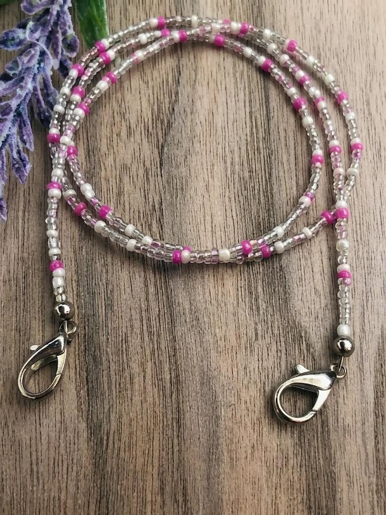 Puede incluir: Un cord&oacute;n de cuentas con un patr&oacute;n repetitivo de peque&ntilde;as cuentas redondas de color blanco opaco, transparente y rosa vibrante. El cord&oacute;n est&aacute; rematado con dos cierres de mosquet&oacute;n de metal plateado en cada extremo para una sujeci&oacute;n segura.