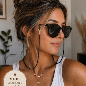 May include: A black beaded glasses chain featuring small, uniform dark beads attached to tortoiseshell sunglasses with silver-toned metal clasps. A circular beige graphic in the corner displays the text MORE COLORS available with a heart icon.