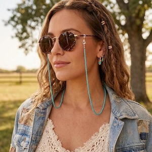 May include: A turquoise beaded eyeglass chain featuring small, uniform round beads attached to the temples of brown tortoiseshell sunglasses with gold-tone metal frames. The chain hangs down in a U-shape from the sides of the eyewear.