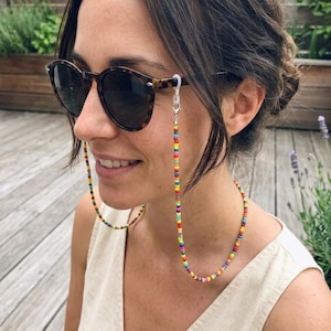 May include: A woman wearing sunglasses with a multi-coloured beaded eyeglass chain. The chain is made of small, round beads in a rainbow of colours, creating a bright and cheerful accessory.