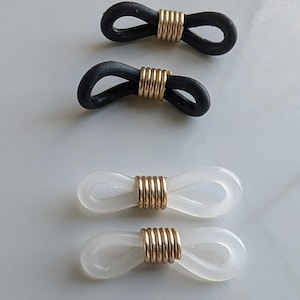 Puede incluir: Cuatro conectores para cadenas de gafas dispuestos en dos filas. Dos conectores est&aacute;n hechos de bucles de goma negra asegurados con una bobina de metal dorado, y dos conectores est&aacute;n hechos de bucles de goma blanca transl&uacute;cida con una bobina dorada.