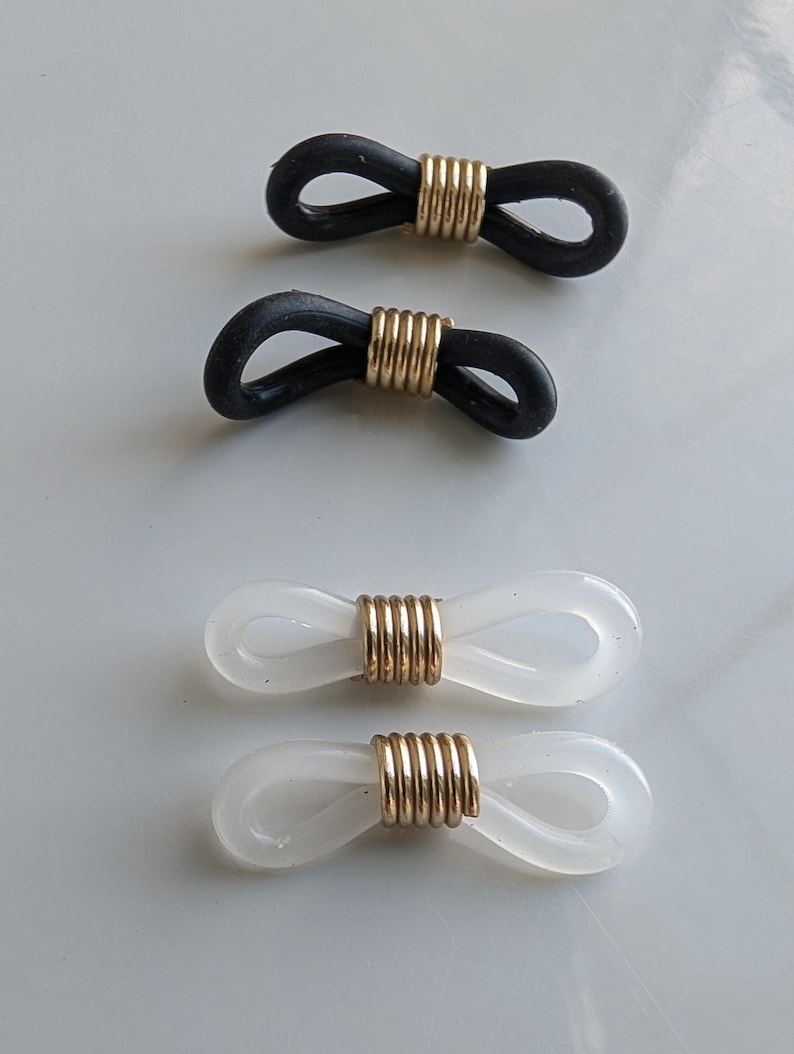 Puede incluir: Cuatro conectores para cadenas de gafas dispuestos en dos filas. Dos conectores est&aacute;n hechos de bucles de goma negra asegurados con una bobina de metal dorado, y dos conectores est&aacute;n hechos de bucles de goma blanca transl&uacute;cida con una bobina dorada.