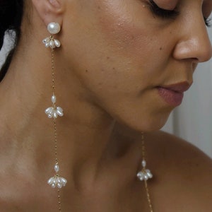 May include: Long gold chain earrings with multiple clusters of small white pearls. The earrings feature a larger pearl at the top of each chain.