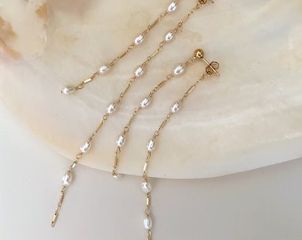 May include: Three pairs of gold dangle earrings with small white pearl beads on a delicate chain.