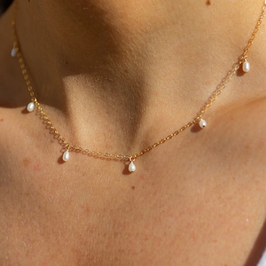 May include: A gold chain necklace with five small white pearl drops hanging from it.