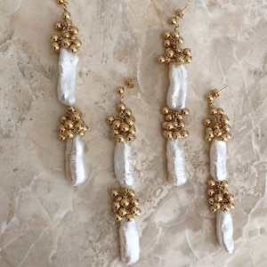 May include: A set of four gold and pearl earrings. Each earring features a long, white pearl drop with two clusters of gold beads.