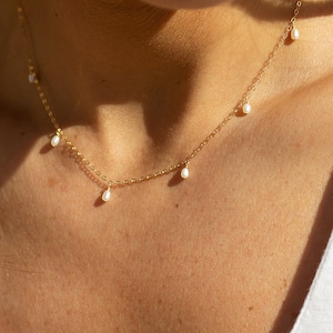 May include: A delicate gold chain necklace with five small white pearl drops hanging from it.
