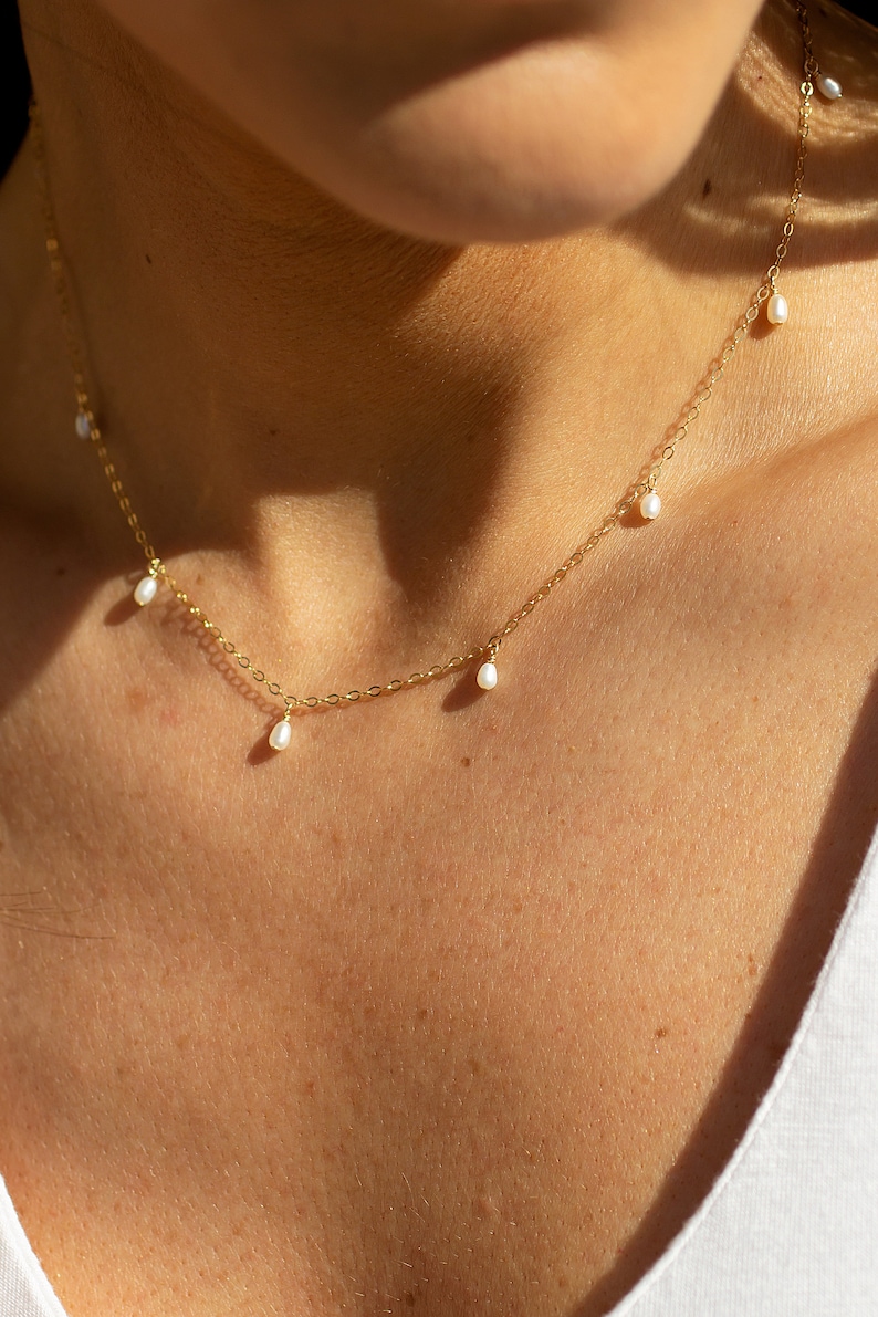 May include: A delicate gold chain necklace with five small white pearl drops hanging from it.