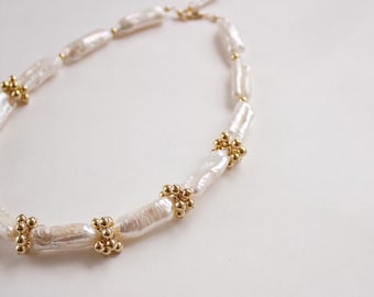 May include: A white pearl necklace with gold accents. The pearls are long and oval shaped. The gold accents are small and round.