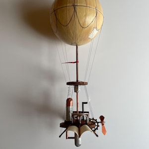 Peut inclure: Un ballon à air chaud steampunk fait main avec un ballon en papier brun, une gondole en bois et un moteur de couleur cuivre. Le ballon a un drapeau rouge attaché au sommet.