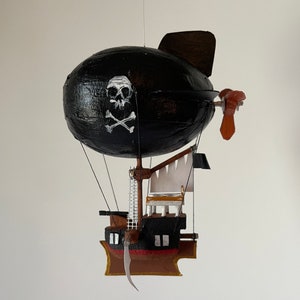 May include: A black and white pirate ship airship with a skull and crossbones design on the balloon. The ship has a white sail and a brown wooden deck.