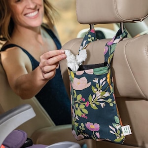 May include: A floral-patterned car tissue holder in a dark teal color, hanging from a car headrest. The fabric features pink, purple, and yellow flowers with green leaves. The holder is filled with white tissues.