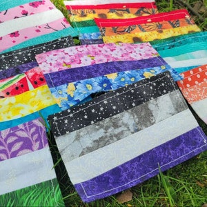 May include: A selection of rectangular fabric items with diverse patterns, such as floral, striped, and geometric designs. The items are displayed on green grass, showcasing a range of colours and textures.