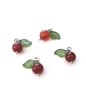 May include: Four red glass cherry charms with green glass leaves. Each charm has a silver loop for attaching to a necklace, bracelet, or other jewelry.