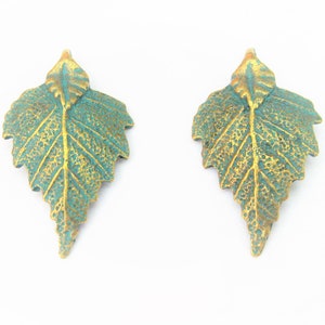 May include: A pair of gold and green leaf-shaped earrings. The leaves have a textured surface and a detailed vein pattern.