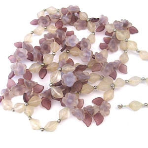 May include: A vintage necklace featuring a floral design with translucent purple, cream, and burgundy flower and leaf-shaped beads. The necklace has a silver-tone clasp and small silver beads between the larger beads.