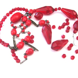 May include: A vintage red beaded necklace with various shapes and sizes of beads. The necklace features faceted, teardrop, and oval beads, along with smaller round beads. The beads are strung together with metal findings.