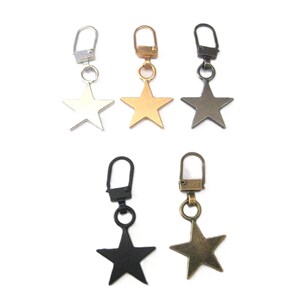 May include: Five zipper pulls with star-shaped charms. The charms are in silver, gold, antique brass, black, and antique gold.
