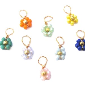 May include: Eight small flower charms made with seed beads and gold wire. The charms are in various colors, including green, blue, yellow, orange, pink, and white.