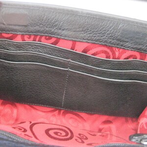 May include: Black leather wallet with a red and black patterned lining. The wallet has multiple card slots and a zippered closure.