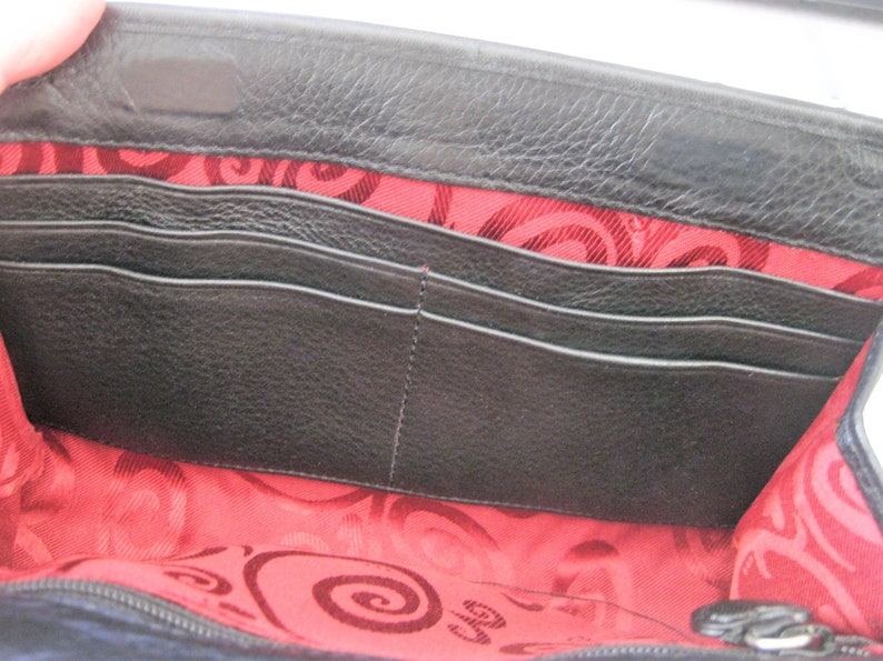 May include: Black leather wallet with a red and black patterned lining. The wallet has multiple card slots and a zippered closure.