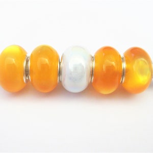 May include: Five glass beads, four are orange and one is white with iridescent shimmer. The beads are strung on a wooden skewer.