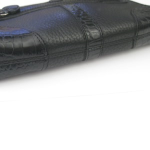 May include: A black leather clutch purse with a textured, crocodile-embossed design. The purse has a single flap closure with a gold-toned buckle.
