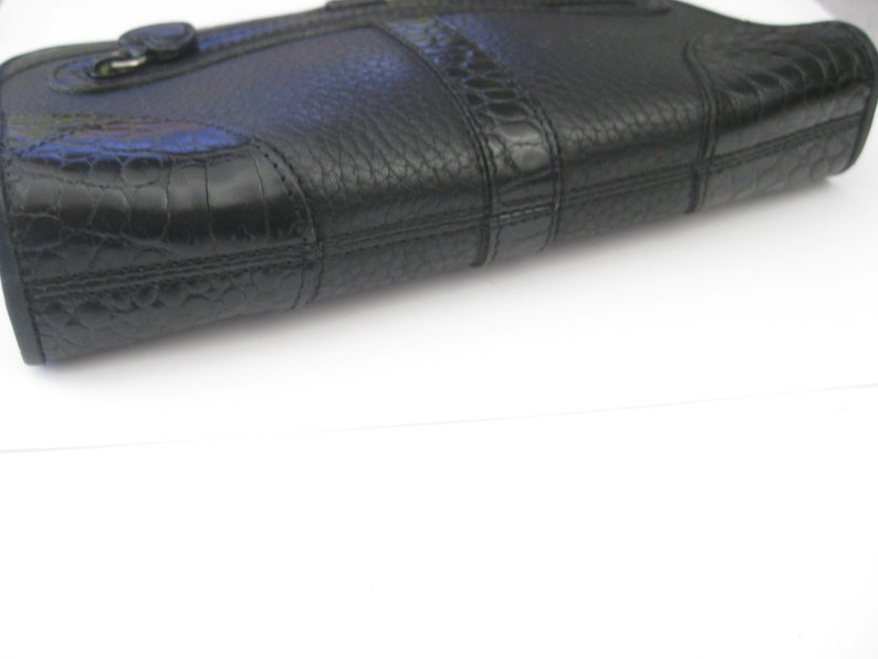 May include: A black leather clutch purse with a textured, crocodile-embossed design. The purse has a single flap closure with a gold-toned buckle.