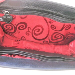 May include: Black leather wallet with a red interior featuring a swirl pattern and the brand name "Betsey Johnson". The wallet has multiple card slots and a zippered compartment.