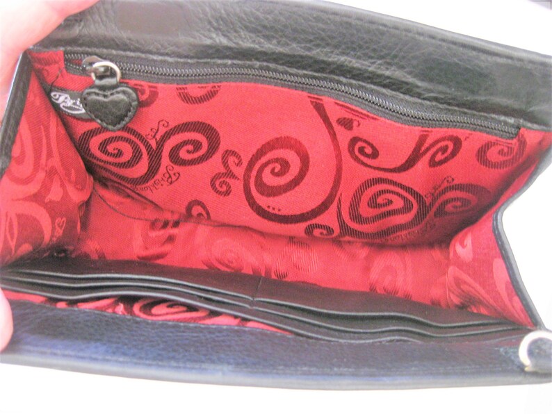 May include: Black leather wallet with a red interior featuring a swirl pattern and the brand name "Betsey Johnson". The wallet has multiple card slots and a zippered compartment.