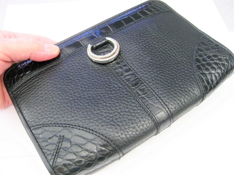 May include: Black leather clutch with a crocodile embossed pattern and a silver ring closure.