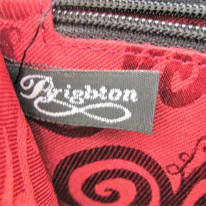 May include: Close-up of a black fabric label with the word "Brighton" in white cursive lettering. The label is attached to a red fabric with a black swirl pattern.