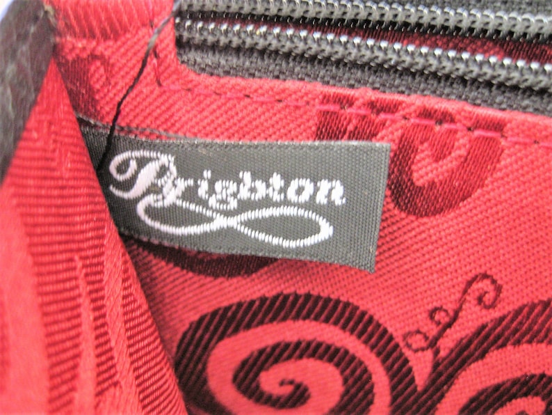 May include: Close-up of a black fabric label with the word "Brighton" in white cursive lettering. The label is attached to a red fabric with a black swirl pattern.