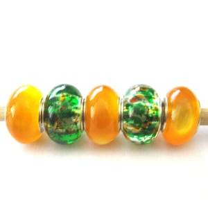 May include: Five glass beads, two are orange and three are green with white flecks. The beads are strung on a wooden skewer.