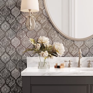 May include: A bathroom vanity with a dark gray cabinet, white marble countertop, and a silver-framed oval mirror. The wall features a patterned wallpaper. A silver sconce with a cream shade is mounted on the wall. A vase of white flowers sits on the counter.