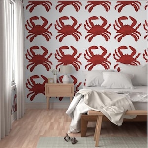 May include: A bedroom with a white wall featuring a repeating pattern of red crabs. The room has a wooden floor, a wooden nightstand, a bed with white bedding, and a wooden bench at the foot of the bed.