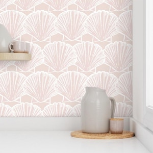 May include: Pink wallpaper with a white seashell pattern. The wallpaper is shown on a wall in a kitchen with a white jug and a small white cup on a wooden coaster.